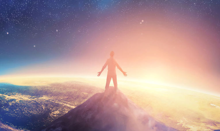a man climbs a high mountain and lifts his arms up in praise